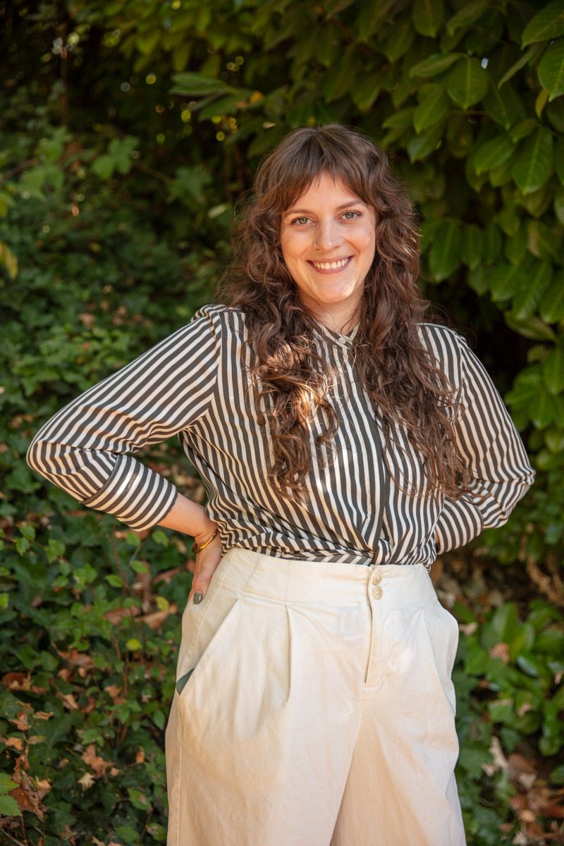 Lexi Walker, therapist and counselor, posing confidently outdoors with greenery in the background, wearing a striped blouse and cream pants
