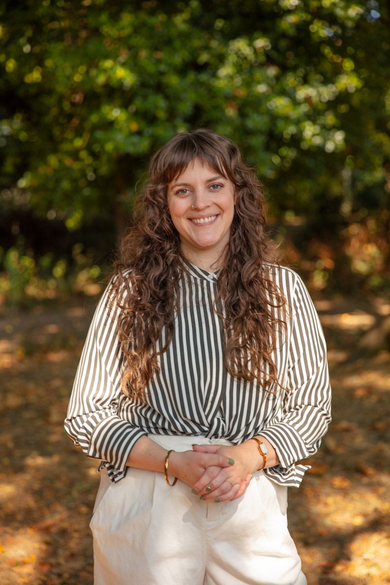Lexi Walker, a counselor with long curly brown hair, smiling warmly while standing outdoors in an autumn setting, wearing a striped blouse